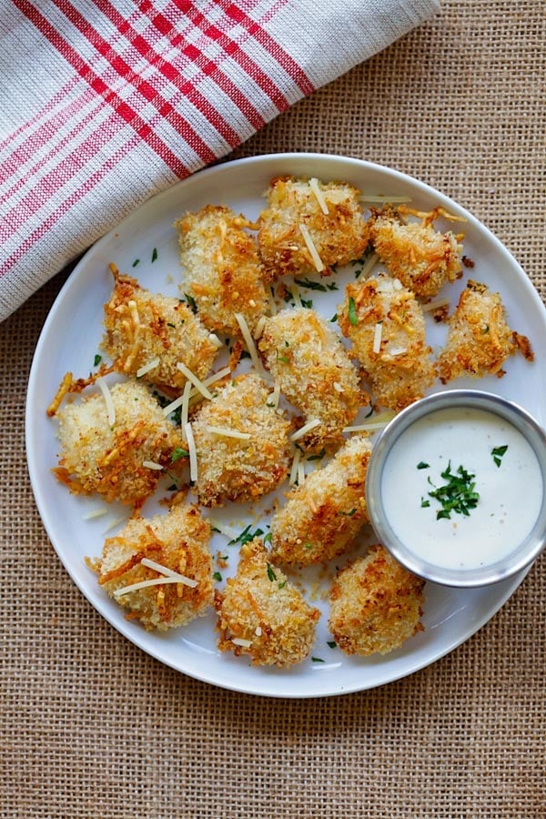 Top down view of homemade easy chicken nuggets recipe with ranch dressing, breadcrumbs and Parmesan cheese in a plate, with a side of dipping sauce.