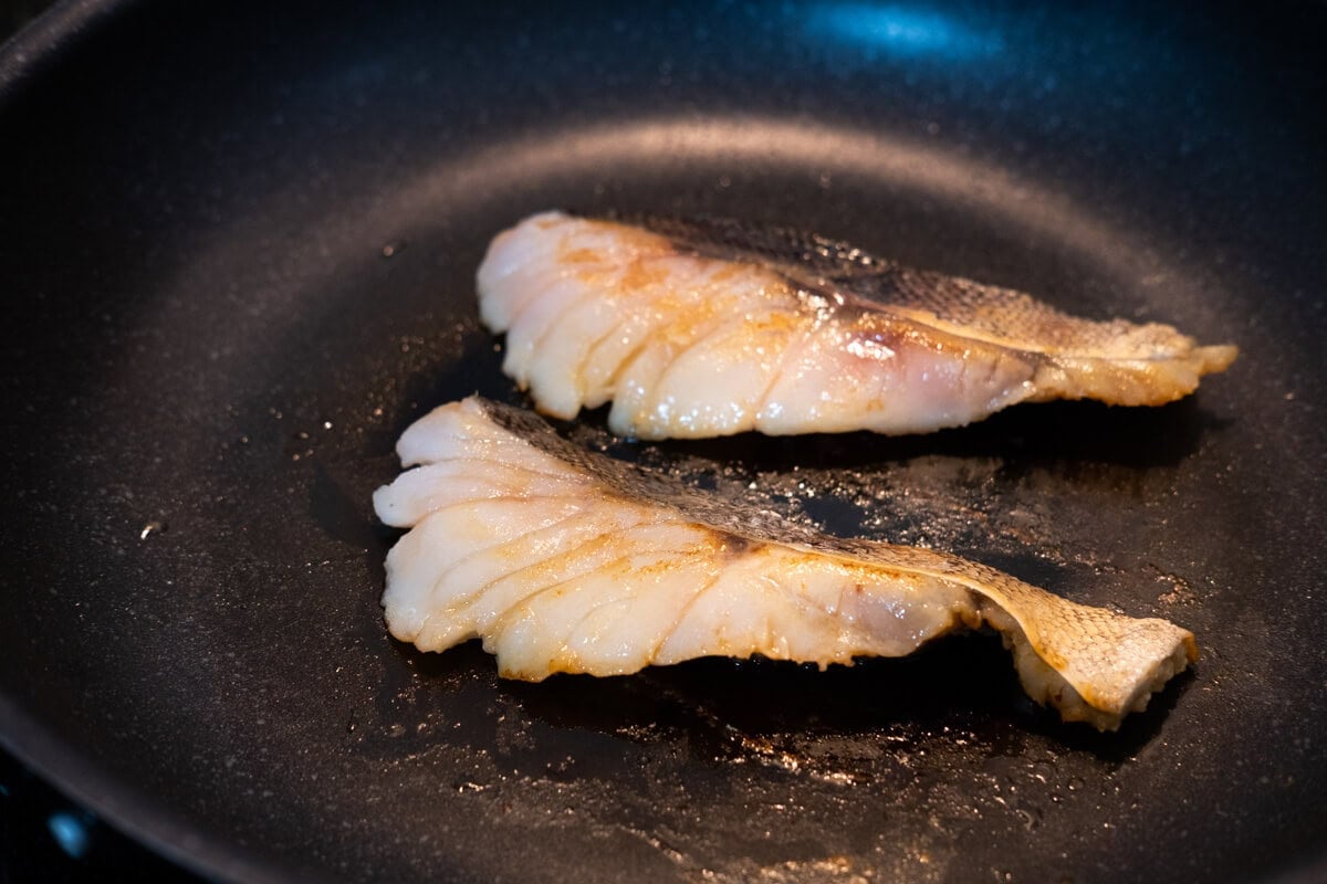 Marinated sea bass being seared on a pan. 