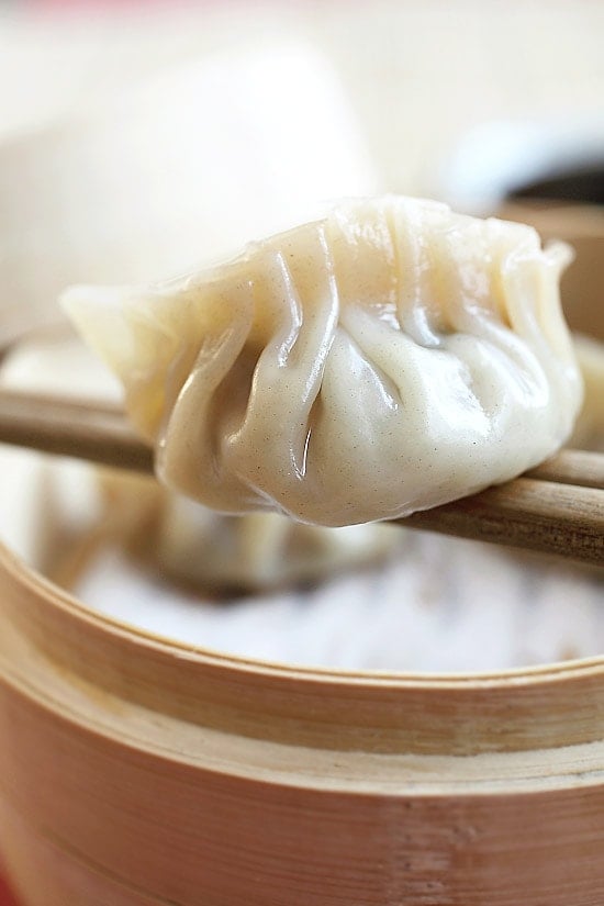 Close up of chopsticks holding a dumpling that's been wrapped and steamed.