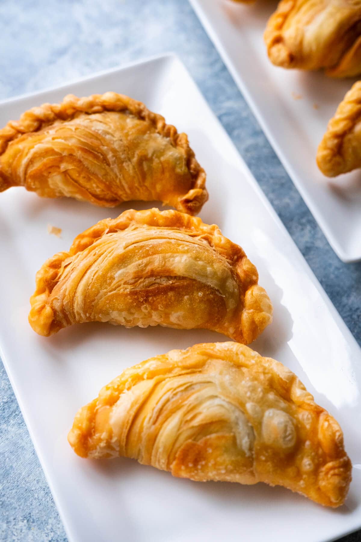 Flaky, golden and crispy homemade curry puffs on a white plate. 