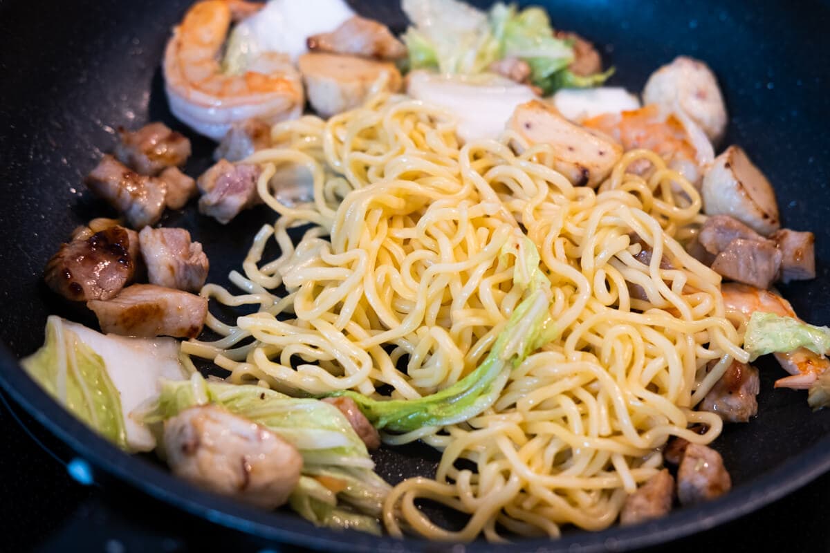 Noodles with pork, fish balls, shrimp, and Napa cabbage in the wok.