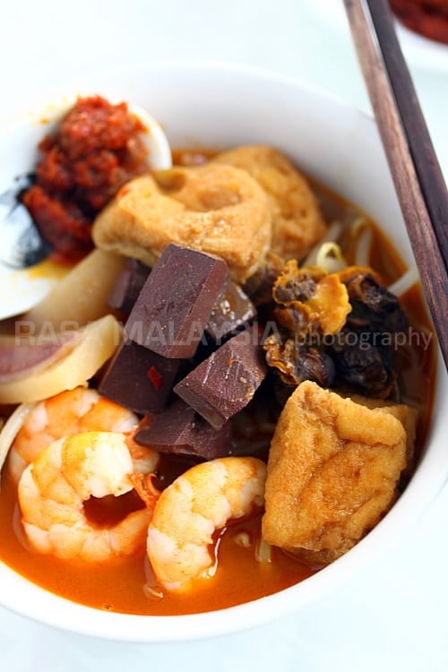 Penang Curry Mee recipe - With toppings many would consider bizarre: pig’s blood cubes (they taste like tofu except that they are maroon in color), bloody cockles, soaked cuttlefish slices, shrimp, and tofu puffs. | rasamalaysia.com