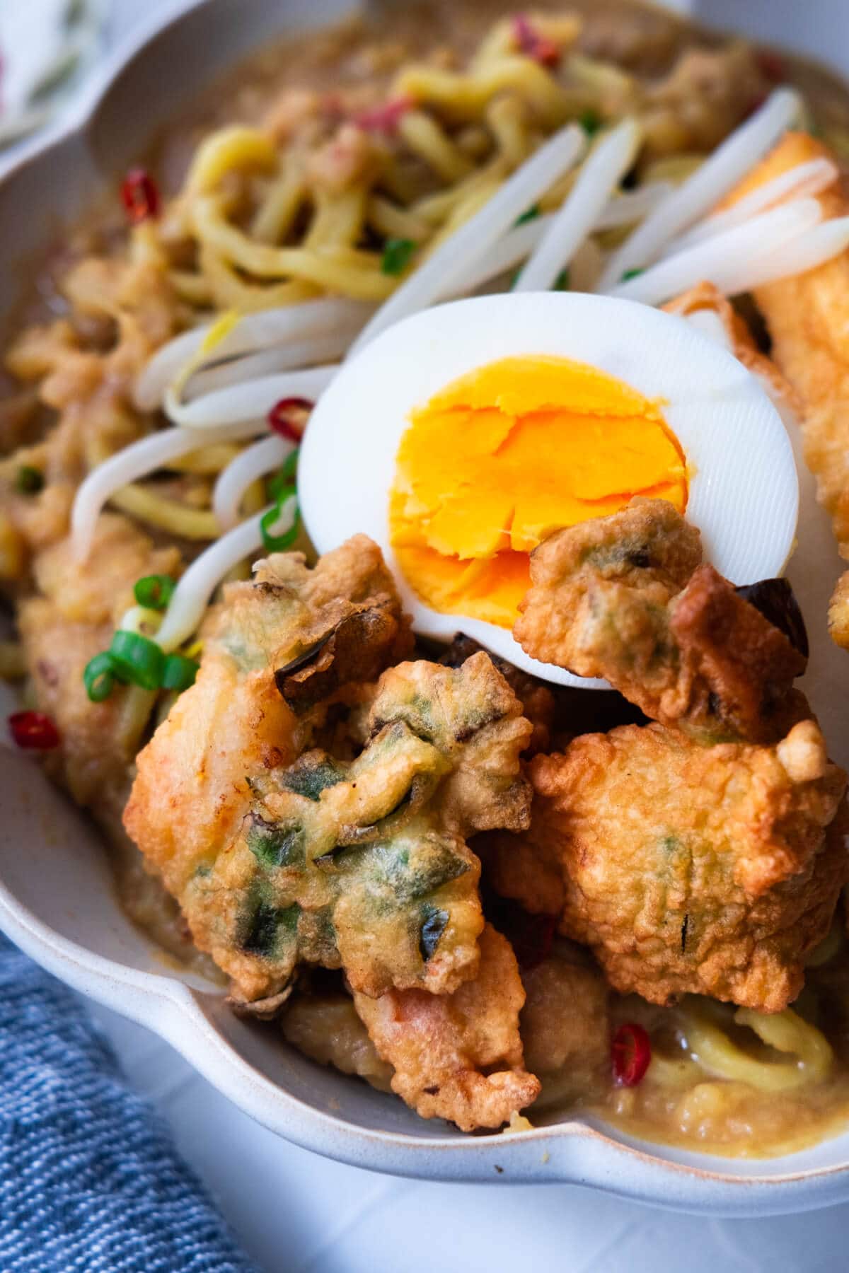 Mee Rebus served with crispy prawn fritters, hard-boiled egg, and bean sprouts.