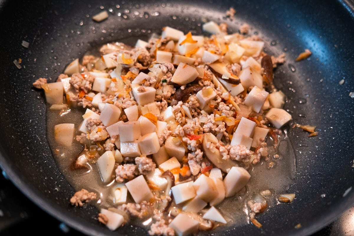 Shallots, garlic, pork, mushrooms, dried shrimp and yam pieces in a wok.