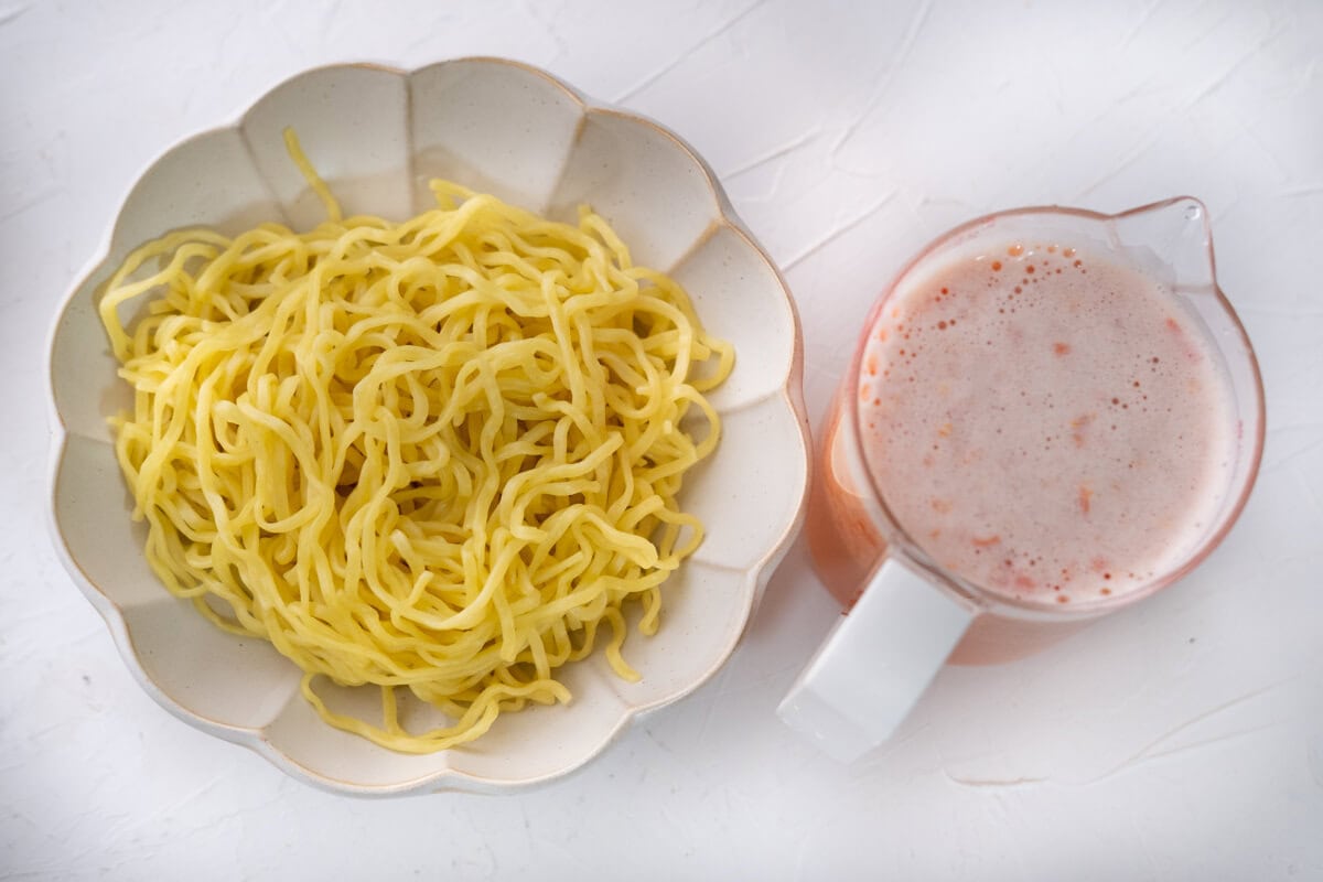 Blended tomato water and blanched yellow noodles in a bowl. 