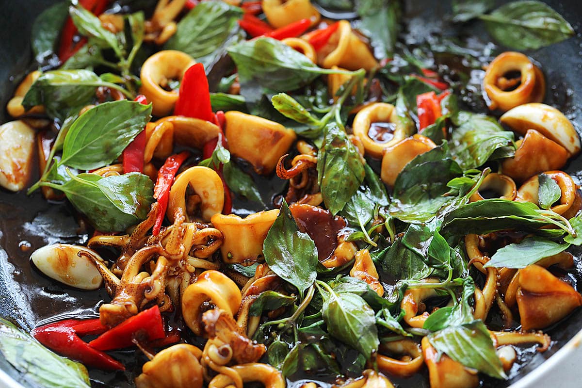 Adding chilies and basil leaves to three cup squid stir fry. 