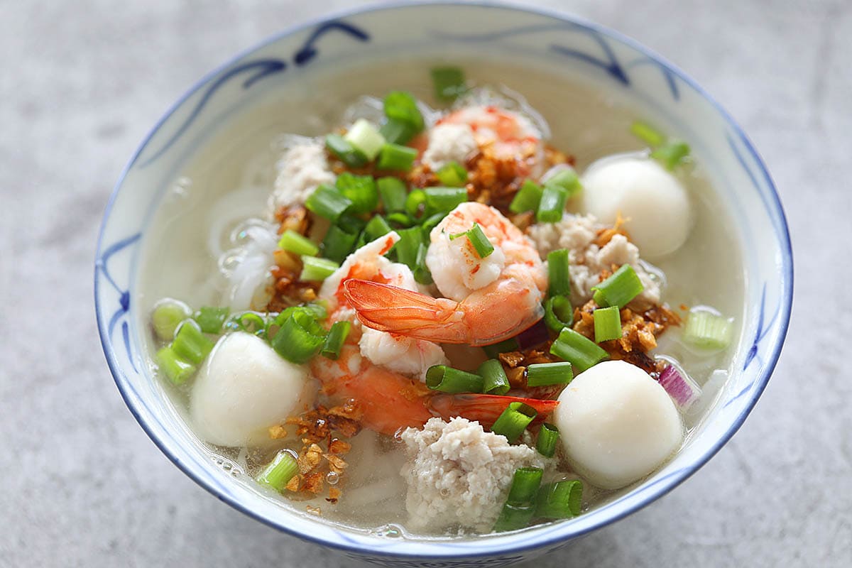 Adding soup to rice noodles in a bowl.