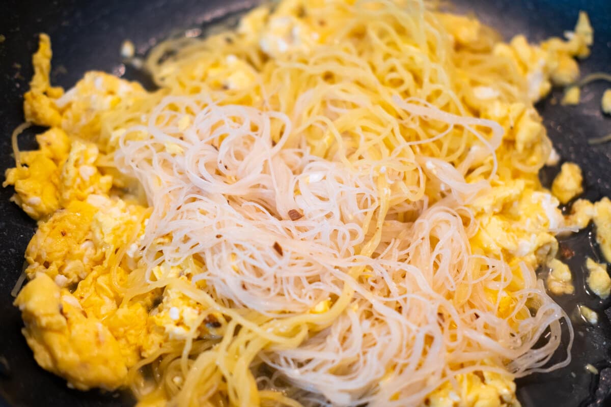 Stir-fry eggs, yellow noodle, and rice vermicelli in a wok. 