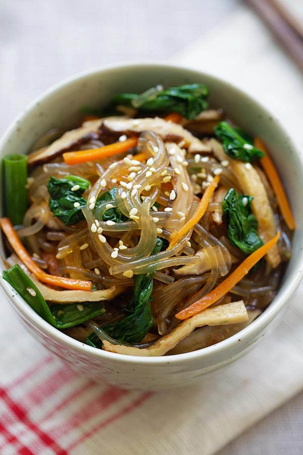 Korean glass noodle dish with sweet potato noodles and vegetables topped with sesame seeds in a bowl.