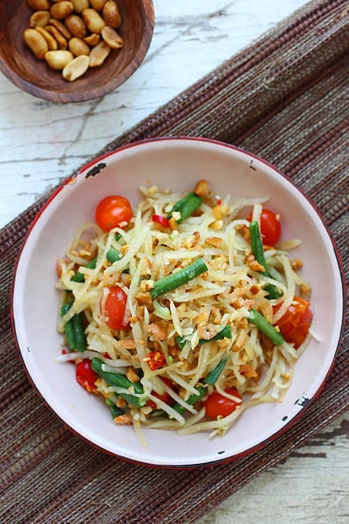 Top down view of low calorie Thai Green Papaya Salad in a plate ready to serve with peanuts, green beans, and tomatoes. 