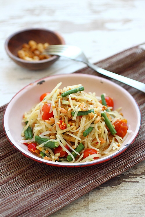 Colorful Papaya Salad with green papaya, peanuts, beans, and tomatoes on table ready to serve. Great Thai recipe.