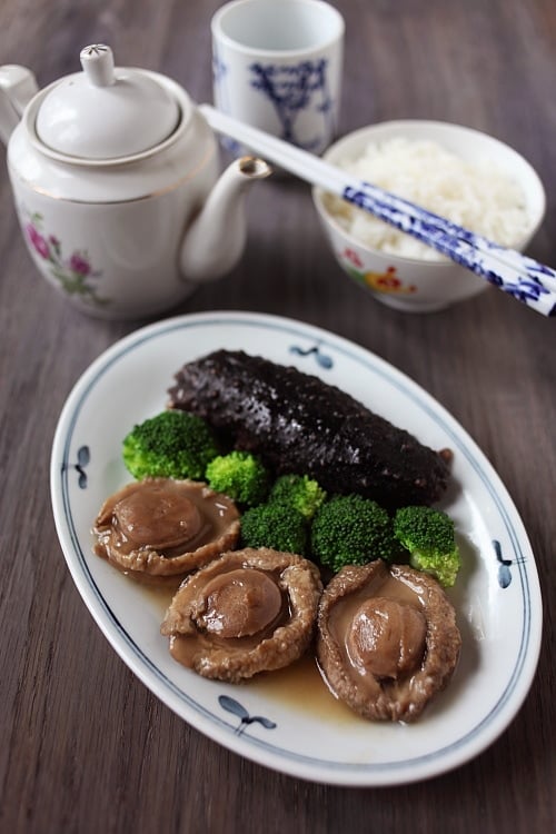 Chinese style braised abalone with sea cucumber in brown sauce with broccoli, served in a serving dish.