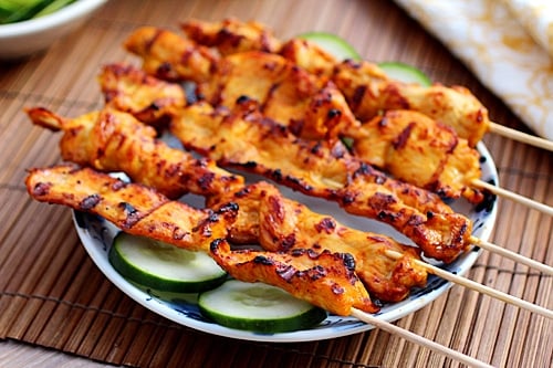 Easy and quick Thai chicken sate skewers served in a plate with slices of cucumbers.