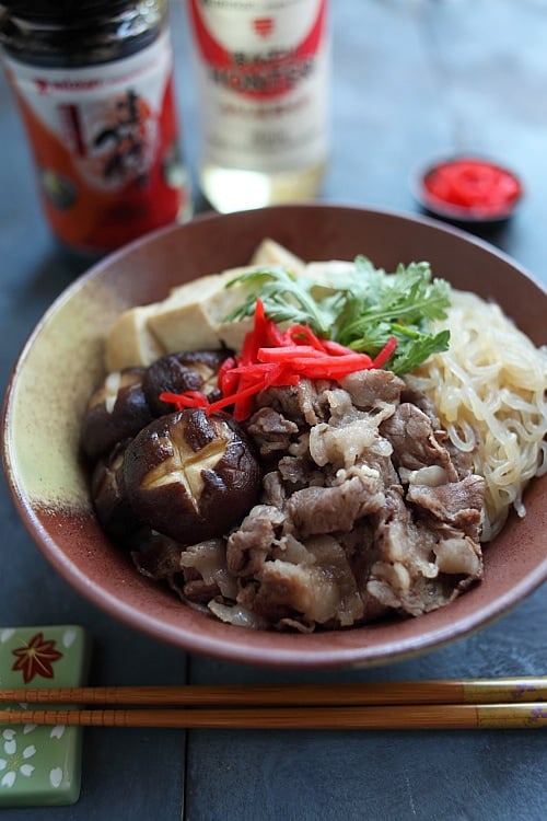 Closed up Japanese sukiyaki donburi rice bowl topped with beef slices, shitake mushrooms, tofu and shirataki noodles.