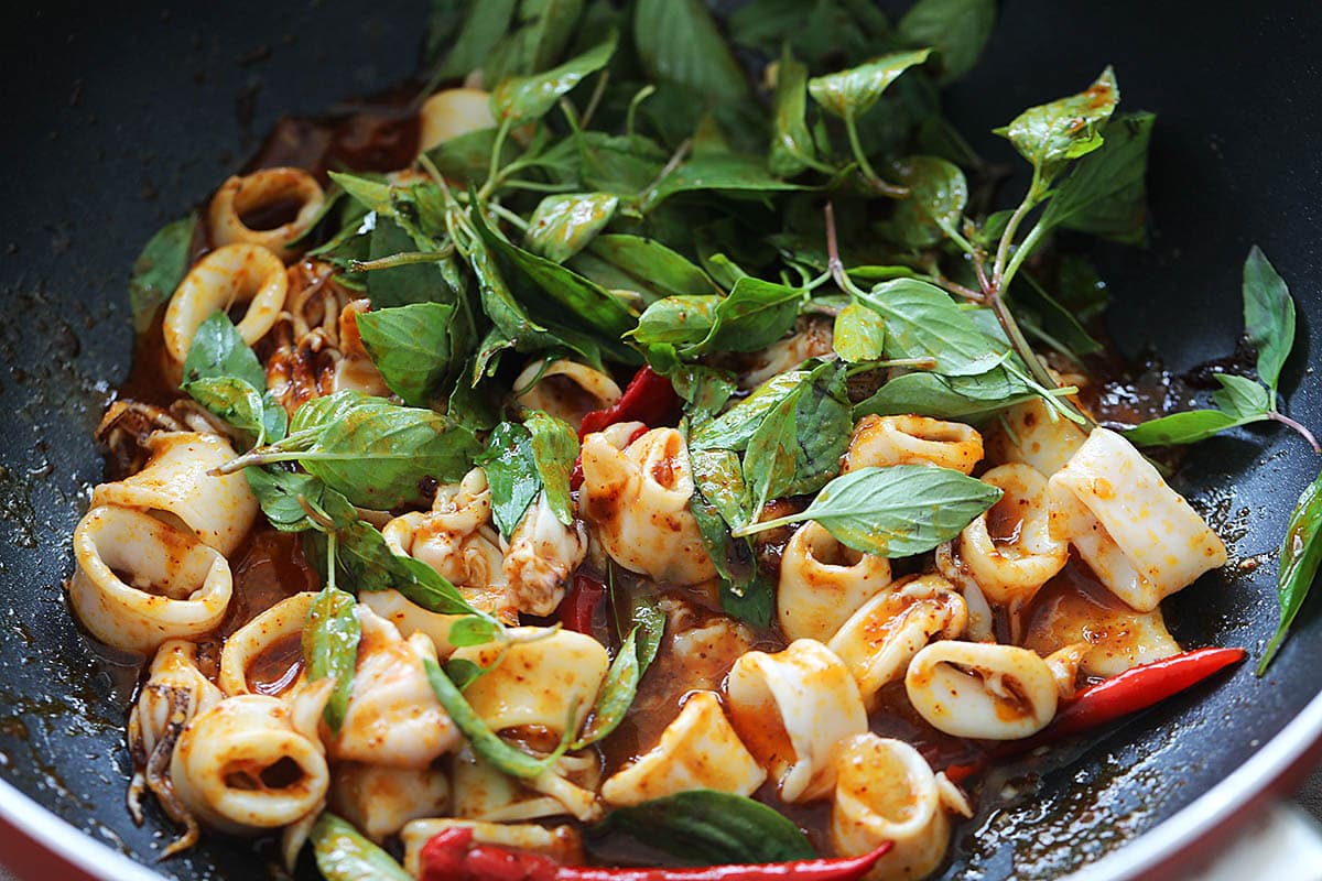 Adding Thai basil leaves to squid to make spicy squid Thai style.