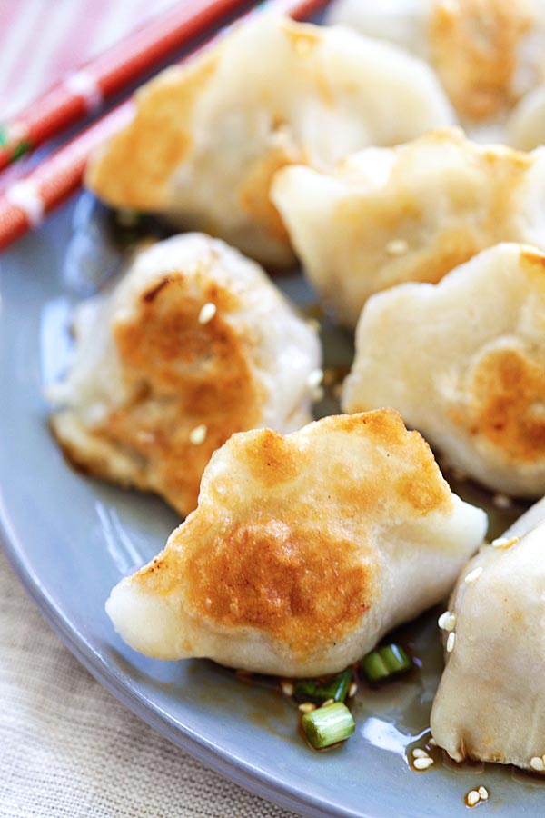 Fried gyoza with chinese black vinegar for dipping garnished with scallions and sesame seeds.