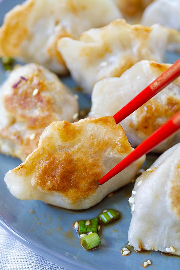 Fried dumpling on plate in ponzu sauce garnished with scallions picked with a pair of chopsticks.