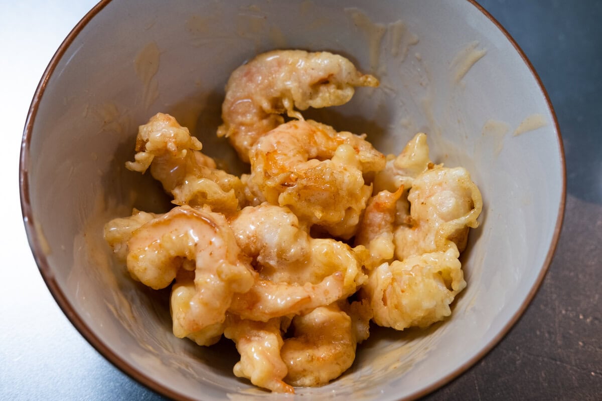 Fried shrimp added into a bowl with dynamite sauce.