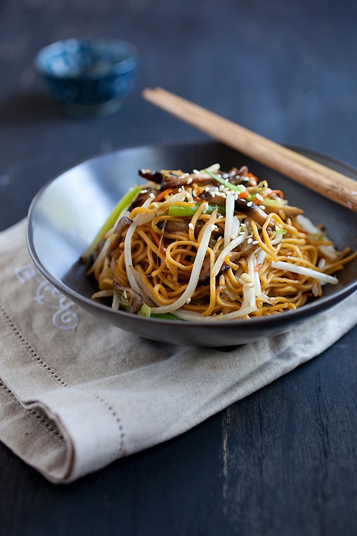 Colorful vegetable chow mein with mushrooms and sprouts in bowl with chopsticks.
