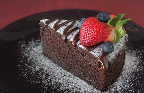 A piece of homemade no bake chocolate cake dusted with flour and decorated with berries.