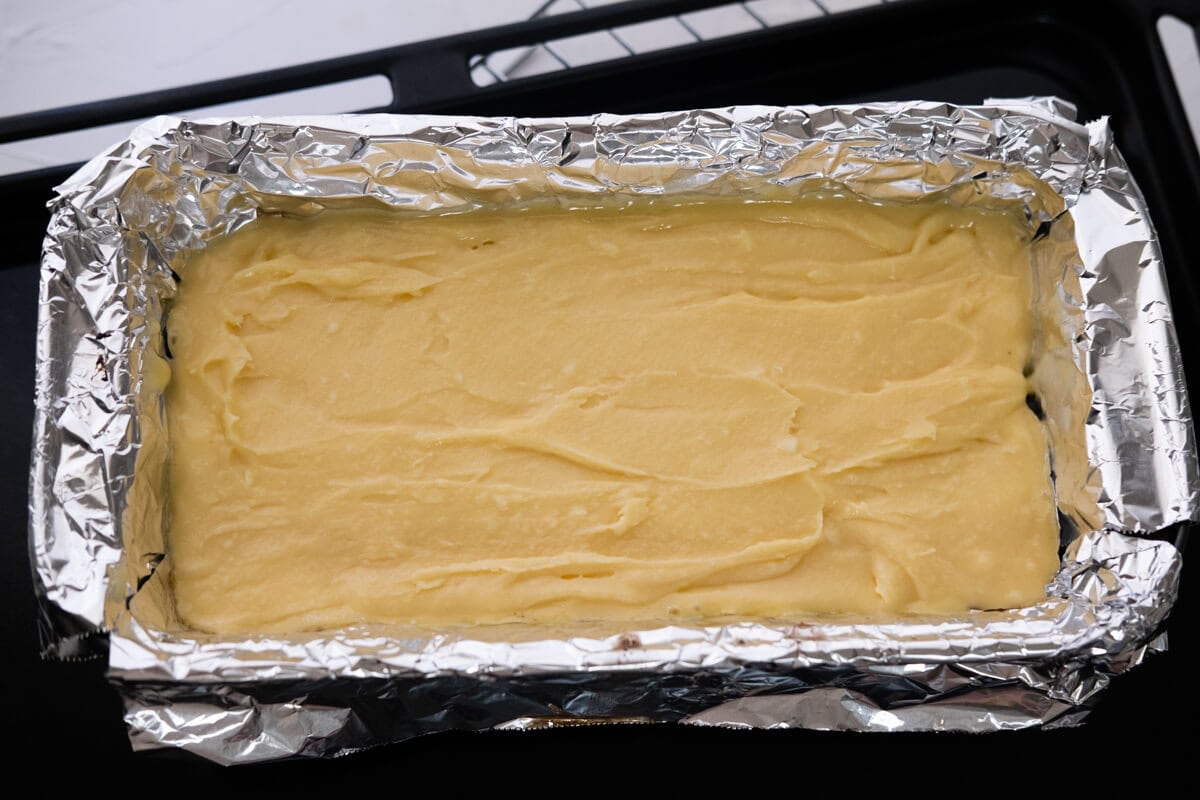 Butter cake batter in a loaf pan with a baked brownie layer.