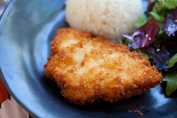 Crispy fried chicken katsu served with rice and salad on a plate.