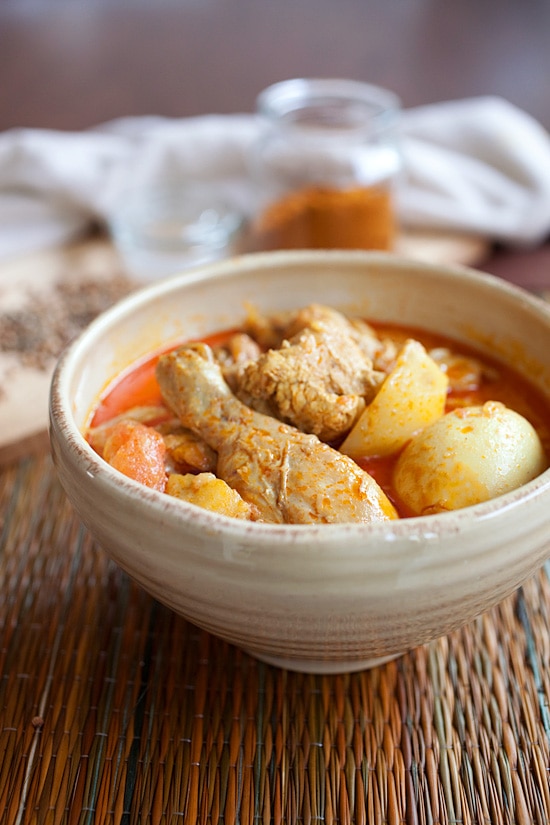 Bowl of Malaysian chicken curry in stoneware bowl on textured placemat.