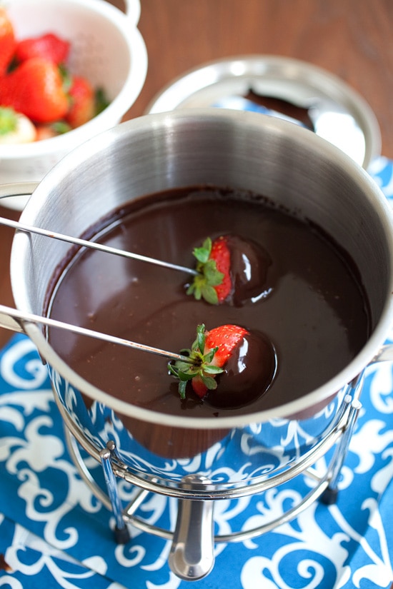 Two fresh strawberries pick in metal skewers dipped into a homemade dark chocolate fondue.