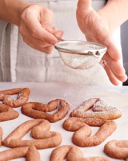Chef dusting confectioners' sugar on easy almond cookies.