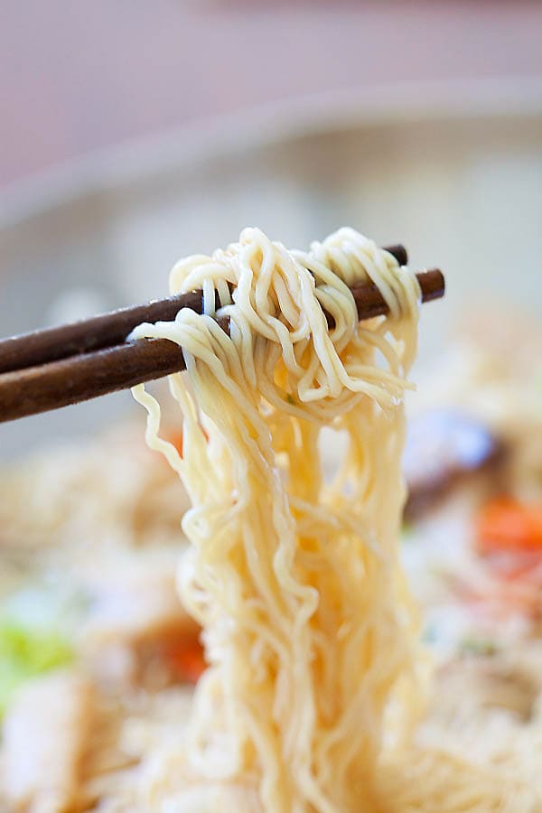 Close up pair of chopsticks picking up homemade lo mein noodles.