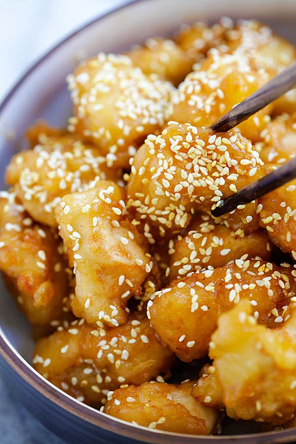 Delicious sesame honey chicken picked up by chopsticks.