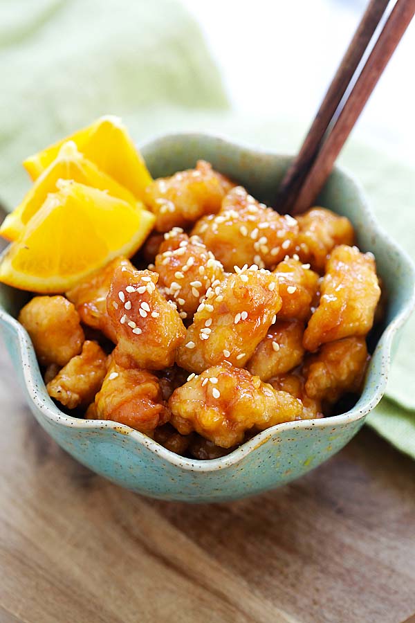 Delicious orange chicken in a bowl complete with lemons and sesame seeds, waiting to be served.