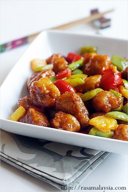 Colorful sweet and sour pork with pineapple and green and red peppers in a serving dish.