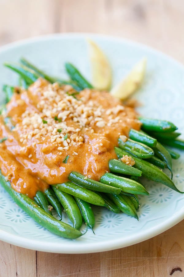 Sauteed green beans with garlic topped with spicy and savory Thai peanut sauce in a plate.