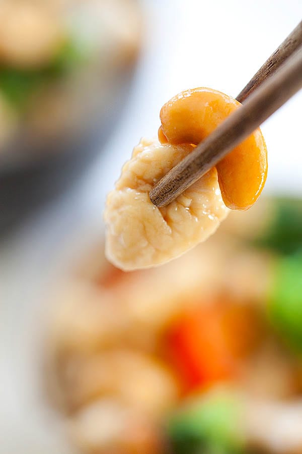 Close up of Asian stir fry chicken and cashew nuts picked with a pair of chopsticks.