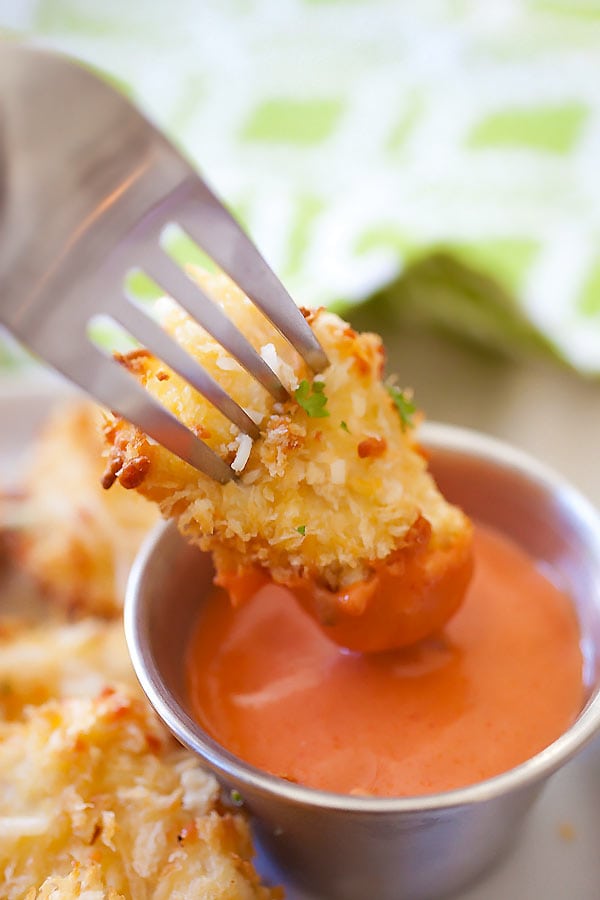 Baked cheesy chicken nuggets covered with panko bread crumbs and Parmesan cheese dipped into spicy ketchup with a fork.
