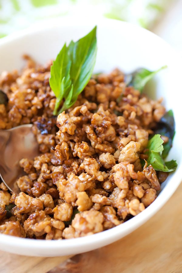 Delicious basil chicken in white bowl garnished with bright green Thai basil.