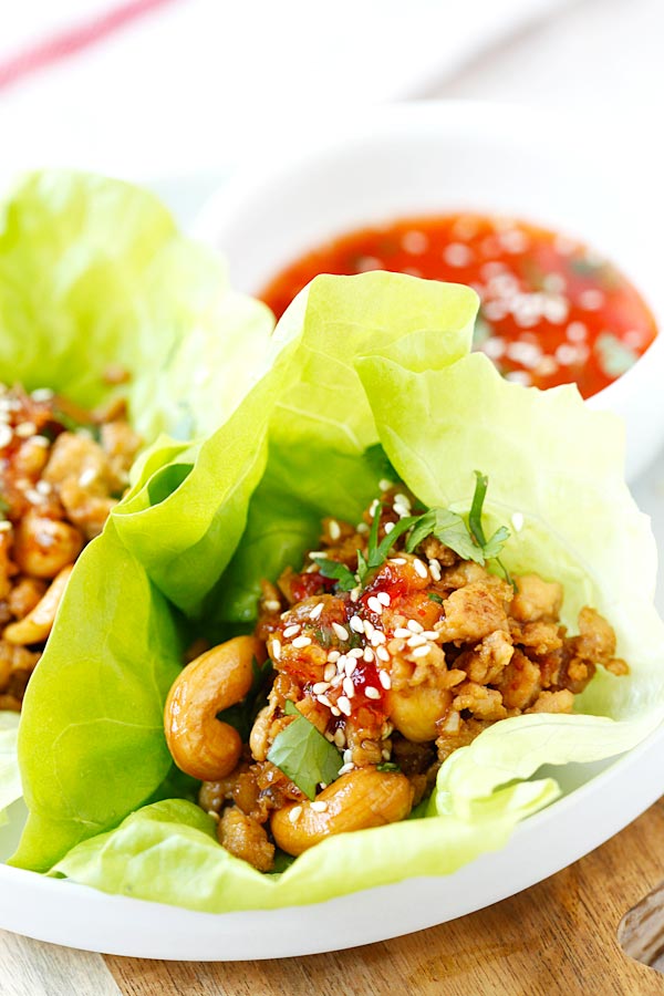 Plated Thai Chicken Lettuce Wrap with cashew nuts, cilantro and sweet chili sauce, adorned with sesame seeds.