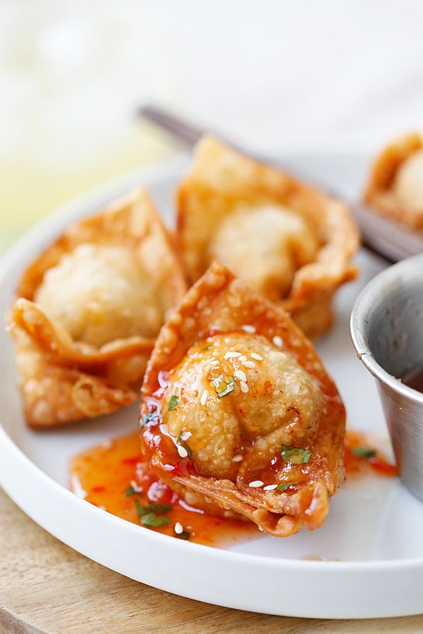 Wonton, fried to golden brown and covered in sweet and sour sauce on plate.