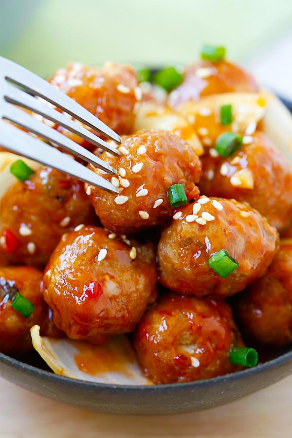 Chinese juicy sweet and sour meatballs with ketchup served with rice, being poked with a fork.