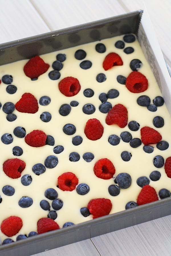 Pre-bake berry cheesecake bars dessert topped with fresh berries in cake pan.