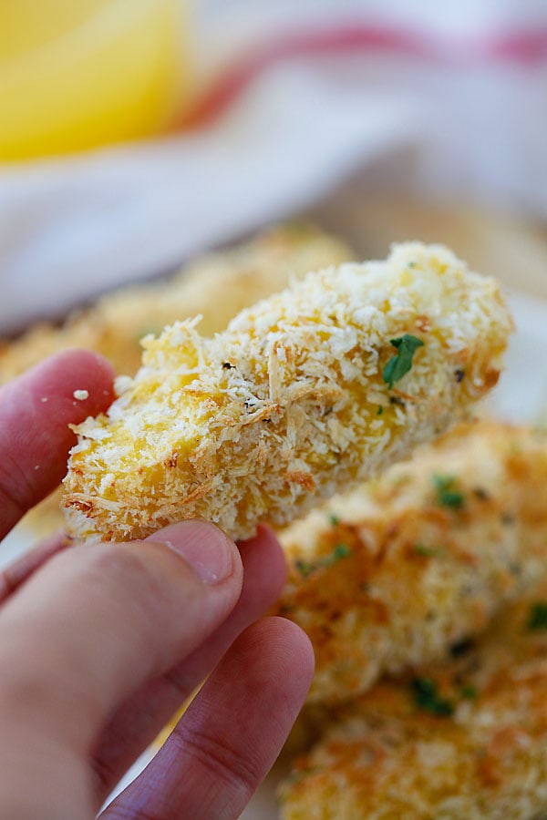 Close up baked mozzarella cheese sticks held in hand.