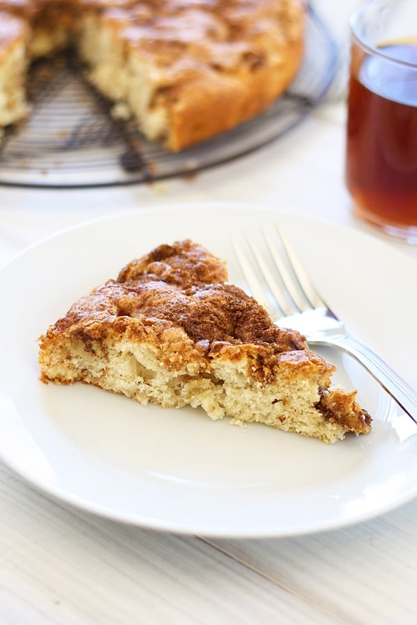 A piece of homemade sweet and decadent coffee cake made with apple served in a plate with a fork.