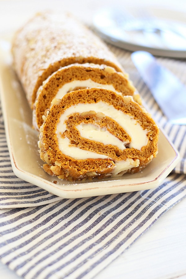 Sliced pumpkin roll cake with sweet cream cheese fillings and covered in crushed walnuts.