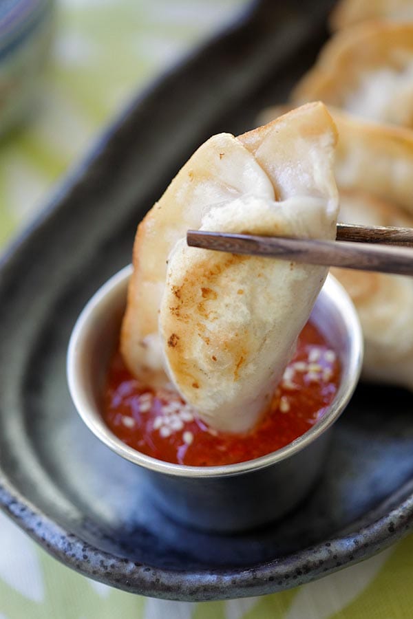 A piece of dumpling picked with a pair of chopsticks dipped into homemade sweet chili sauce.