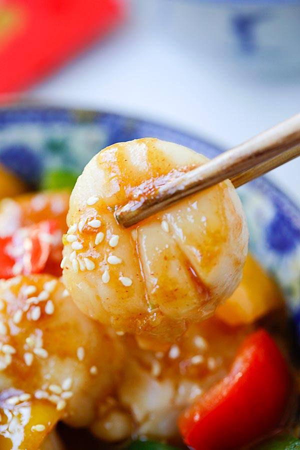 Close up Szechuan Scallops in brown Szechuan sauce picked with a pair of chopsticks.