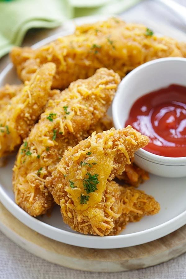 Baked Garlic Cheddar Chicken Strips with cheddar cheese and garlic in a plate with a side of dipping sauce.