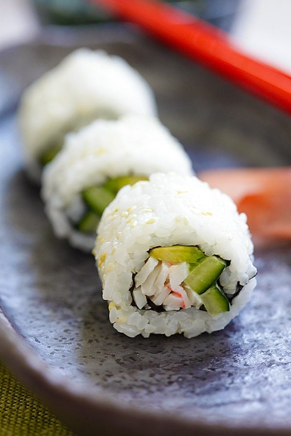 A California roll sushi recipe cut into 3 pieces, ready to serve with chopsticks.