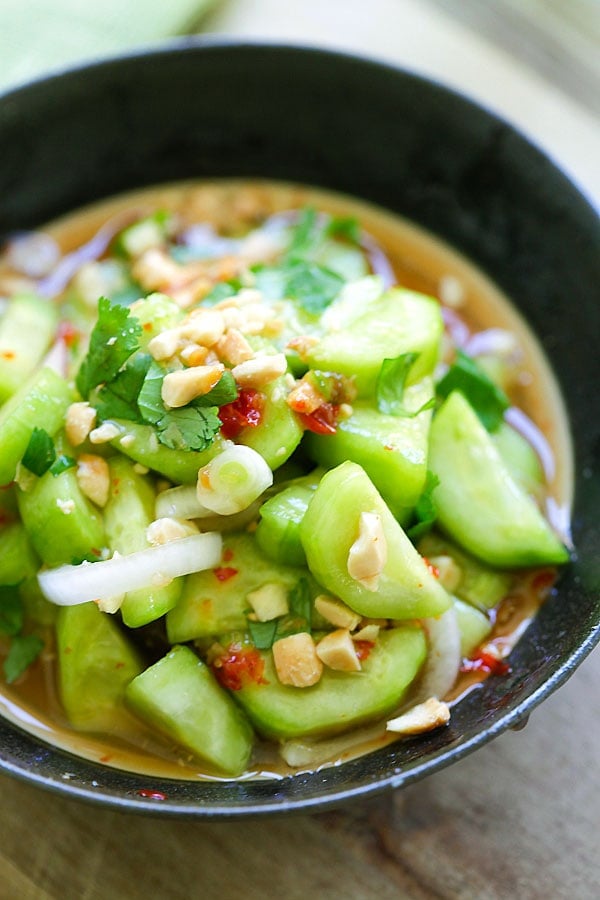 Easy and delicious Thai Cucumber Salad in a bowl ready to serve with peanuts, onions, and cilantro in yummy sauce.