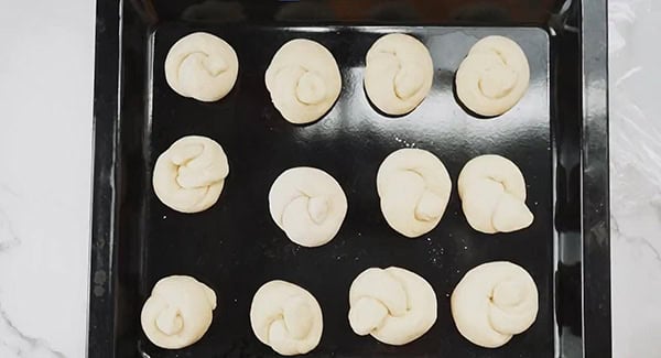 Dinner roll knots on a baking tray.